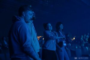 Uczestnicy wydarzenia, zadowoleni, stojący w ciemnej sali oświetlonej niebieskim światłem scenicznym podczas eventu Brill AV Media 2025.
